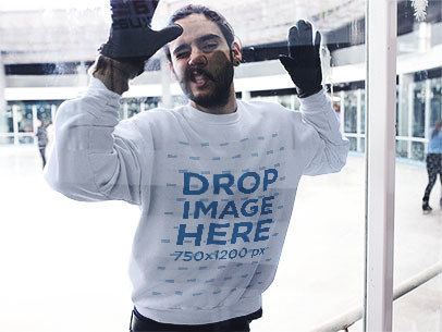 Funny Guy Against a Glass Wearing a Crewneck Sweatshirt at an Ice Skating Rink a13256