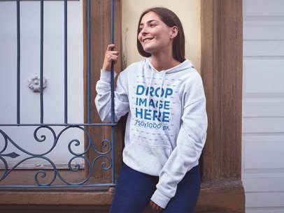 Smiling Pretty Woman Wearing a Pullover Hoodie Mockup Sitting on a Small Ledge