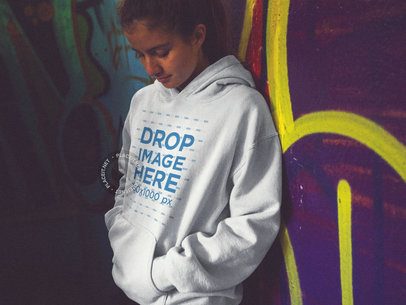 Woman Wearing a Pullover Hoodie Mockup Leaning on a Graffiti Street Wall
