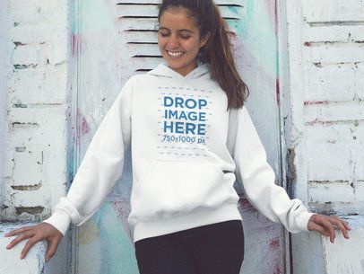 Smiling Young Woman Wearing a Pullover Hoodie Mockup Against a White Wall