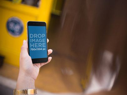 Mockup Of A Woman Holding A Black iPhone On Her Left Hand Over Shoulder
