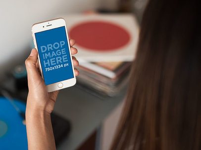 Young Woman Holding an iPhone on her Left Hand While At Her House Mockup