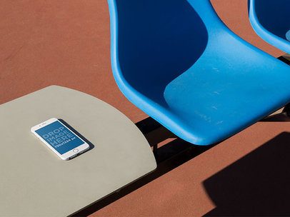 White iPhone 6 Lying Over A White Table Near A Blue Plastic Chair Mockup a14095