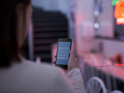 Over Shoulder Mockup Of A Girl Looking At Her iPhone 6 While At A Diner Restaurant With Red Lights On The Background a13998
