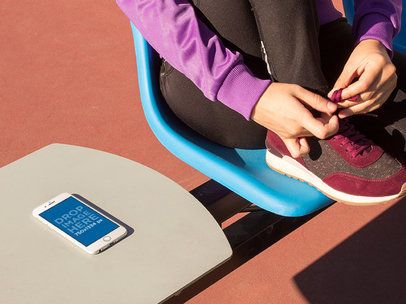 Mockup Of A White iPhone 6 Lying Over A Table While A Girl Is Tying Her Laces In A Plastic Chair a14094