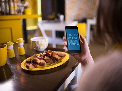 Mockup Of A Woman Holding An iPhone On Her Right Hand While About To Have Breakfast
