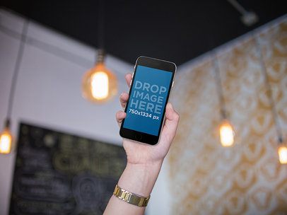 iPhone Being Held By A Womans Hand Inside A Room With Hanging Lamps Mockup a14006