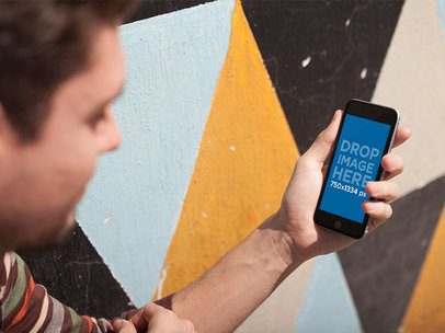 Young Dude Using His Smartphone While Crouching Near A Colorful Wall In The City Mockup a14125