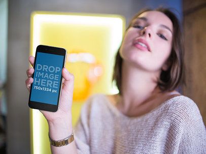 Mockup of a Young Woman Holding an iPhone While Posing Inside a Shop a14007