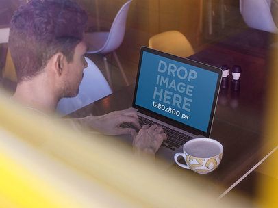 Through The Window Mockup Of A Young Man Having A Coffee While Using His MacBook Pro
