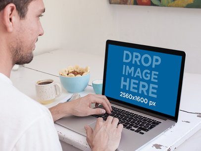 Over-the-Shoulder Mockup of a Man Using a Macbook Pro at a Table