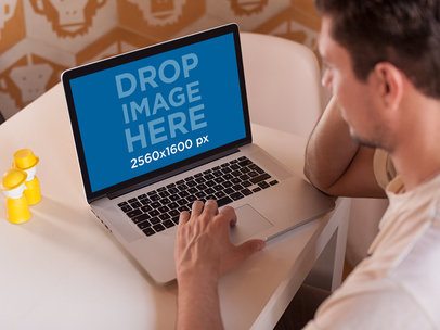 Young Man Using His MacBook Pro While Sitting On His Table Mockup