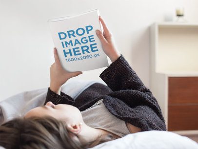 Young Woman Looking at a Book Cover While Lying down in Her Bed Mockup