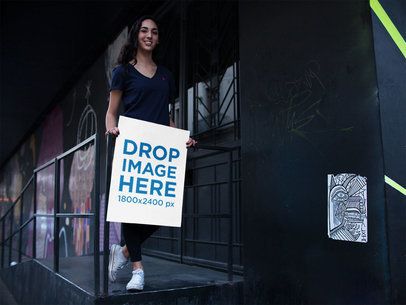 Mockup of a Happy Woman Holding a Poster While in the Street