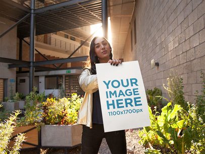 Young Woman Wearing a Shiny Golden Jumper Holds a Poster While in a Terrace With Plants Mockup