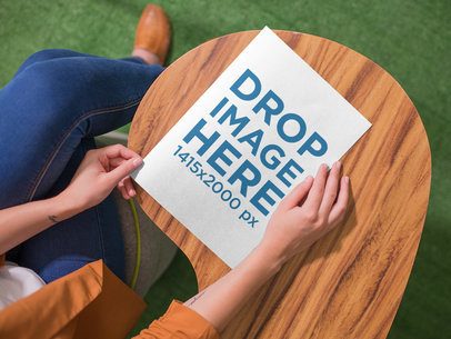 Mockup of a Woman About to Open a Booklet While Sitting Down in a Wooden Desk