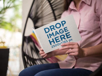 Young Woman Reading a Small Catalog While Sitting Down in an Acapulco Chair Mockup