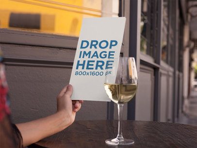 Urban Restaurant Menu Booklet Mockup Held on a Wooden Table With a Glass of White Wine