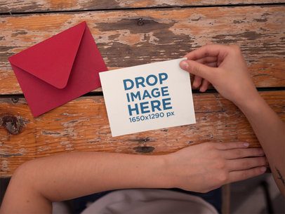 Invitation Template Held Near a Red Envelope on an Old Wooden Table