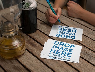 Woman About to Write on a Postcard Mockup While Other Postcards Lying on a Wooden Table