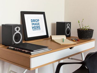 Art Print Mockup on a Black Frame Lying on a Wooden Desk Near Speakers a14691