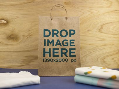 Paper Bag Standing Near T-Shirts Against a Wooden Background