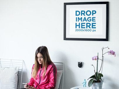Young Woman Sitting Down Near a Framed Art Print Template on a White Wall