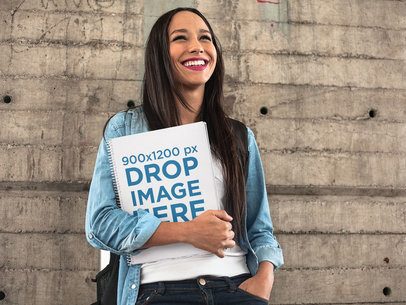 Happy Pretty Woman Holding a Spiral School Notebook Template While Against a Concrete Wall
