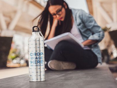 Woman Sitting Down Reading With an Aluminum Water Mockup Bottle Near Her